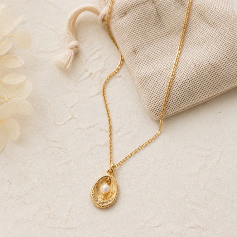 Gold-plated pendant necklace with a freshwater pearl beside a small linen pouch.